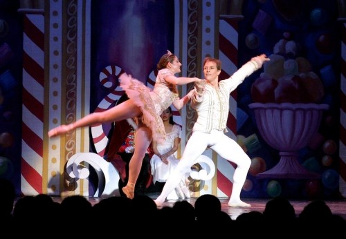 A ballet performance featuring a male and female dancer in elegant costumes, set against a colorful, festive backdrop.