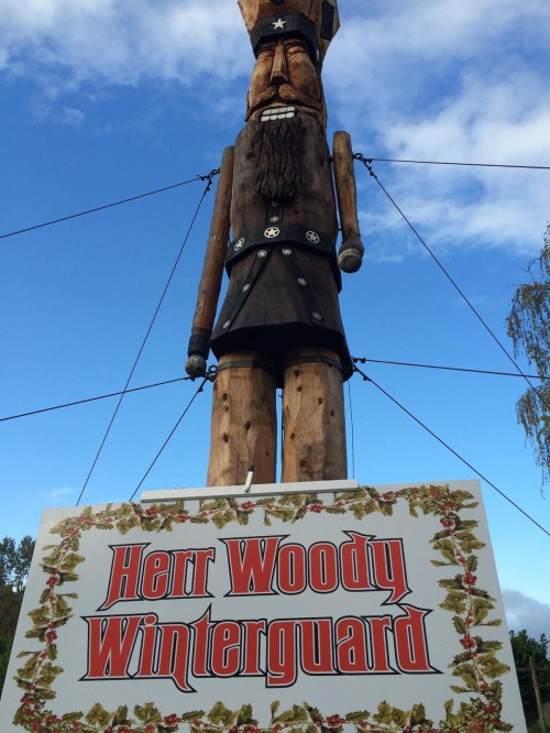 A tall wooden nutcracker figure stands above a sign that reads "Herr Woody Winterguard" against a blue sky.