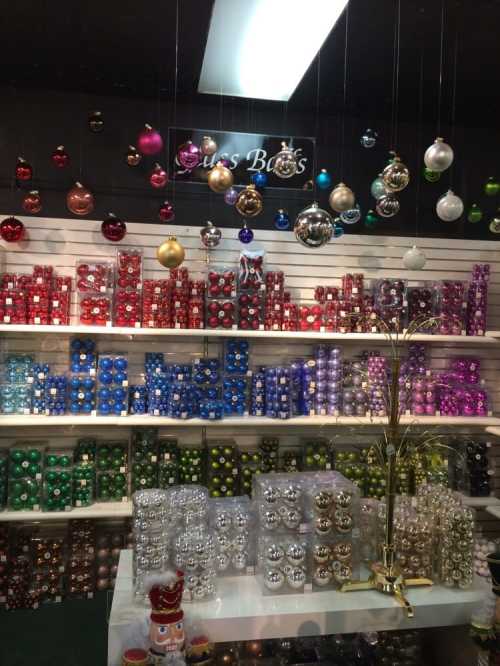 A display of colorful Christmas ornaments in various shapes and sizes, arranged on shelves with a festive atmosphere.