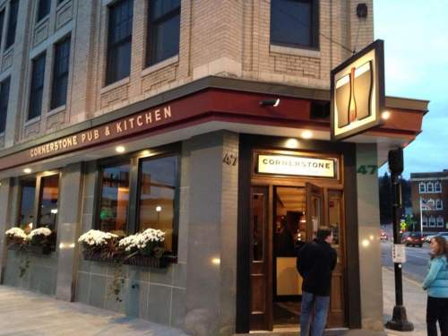 Exterior of Cornerstone Pub & Kitchen, featuring a welcoming entrance and decorative flowers, during twilight.