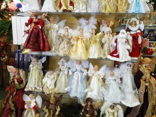 A display of various angel figurines in elegant dresses, featuring different colors and styles, arranged on shelves.