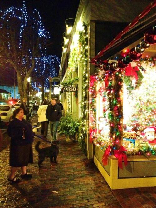 A festive street scene with holiday lights, a decorated shop window, and a woman walking a dog.