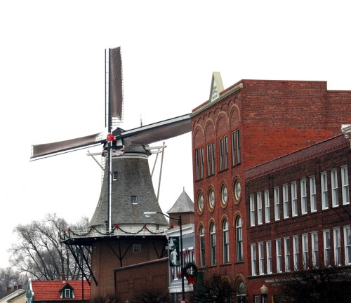 A traditional windmill beside a brick building, set against a cloudy sky.