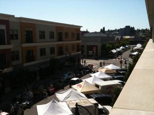 A view of a street market with tents and vendors, surrounded by buildings under a clear blue sky.