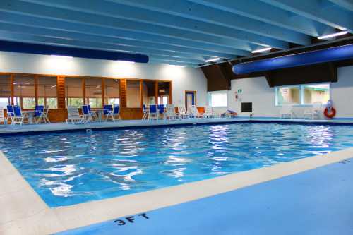 Indoor swimming pool with blue walls, clear water, and lounge chairs around the edge.