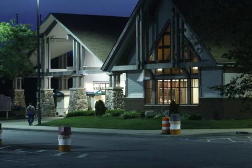 A well-lit building at dusk, featuring a stone facade and large windows, with a person walking nearby.