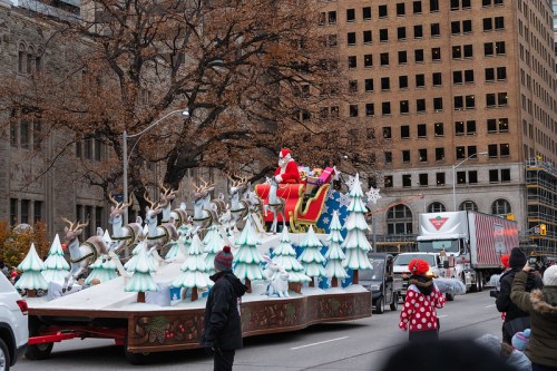 A festive parade float featuring Santa in a sleigh, surrounded by reindeer and decorated Christmas trees.