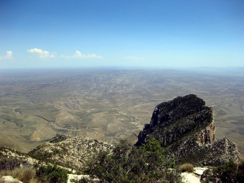 A panoramic view of a vast desert landscape with distant mountains under a clear blue sky.