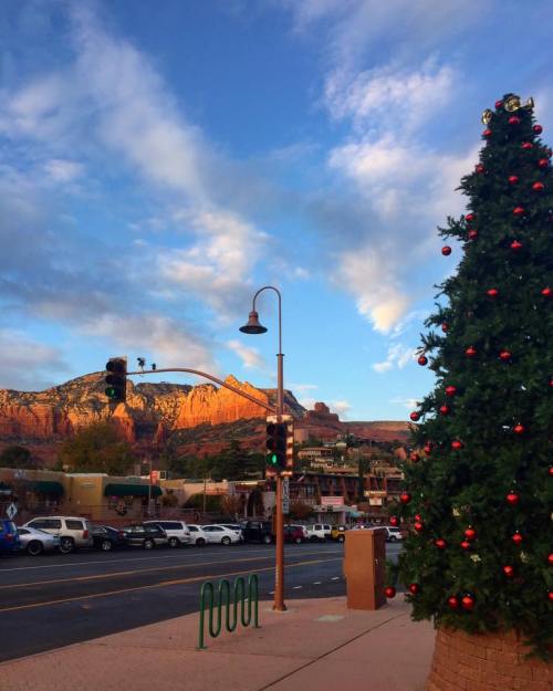 A festive Christmas tree stands beside a street with mountains and a colorful sky in the background.
