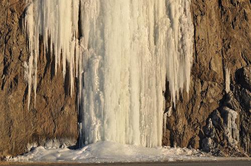 A frozen waterfall cascading down a rocky cliff, with icicles hanging and ice forming at the base.