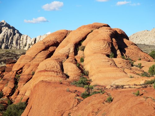 A rugged, orange rock formation with layered textures under a blue sky and scattered clouds.