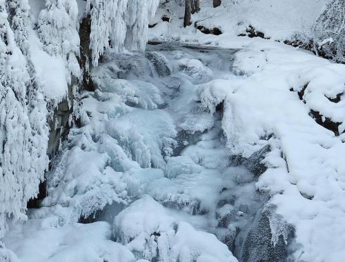 A frozen stream surrounded by snow-covered rocks and icicles, creating a serene winter landscape.