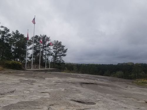 A rocky landscape with several flags on poles, surrounded by trees under a cloudy sky.