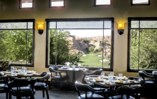 Elegant restaurant interior with tables set for dining, featuring large windows overlooking a scenic golf course.
