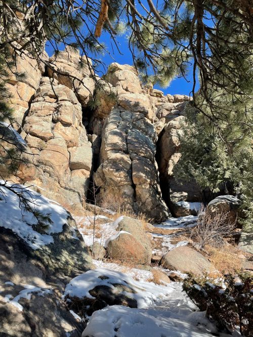 Rocky terrain with large boulders, sparse vegetation, and patches of snow under a clear blue sky.