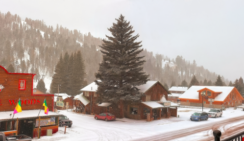 Snowy mountain village scene with wooden buildings, pine trees, and a road, creating a cozy winter atmosphere.