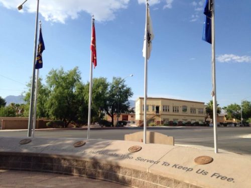A memorial with flags honoring those who served, set against a clear blue sky and a building in the background.