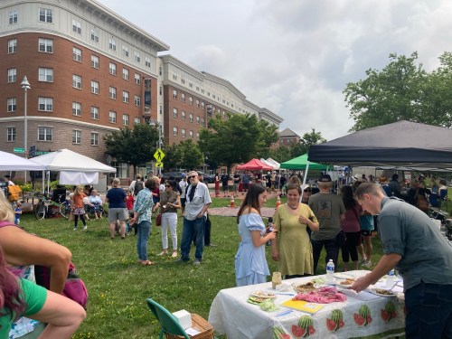 A bustling outdoor market with tents, food stalls, and people enjoying the event in a grassy area.