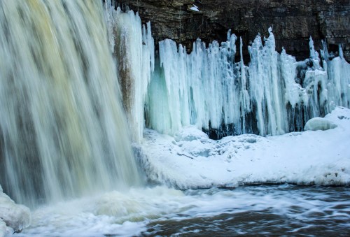 A waterfall cascading over icy rocks, surrounded by frozen ice formations and snow.