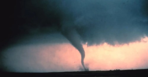 A tornado touches down in a dark sky, with a gradient of colors from gray to orange at the horizon.