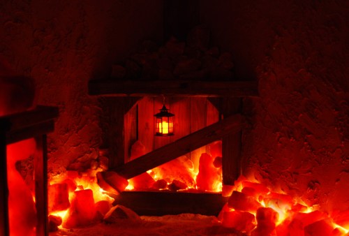 A cozy, dimly lit space with a lantern hanging above a wooden shelf, surrounded by glowing salt rocks.