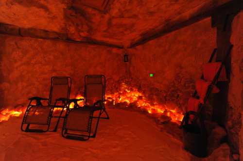 A tranquil salt room with two reclining chairs, illuminated by soft orange lights and surrounded by salt-covered walls.