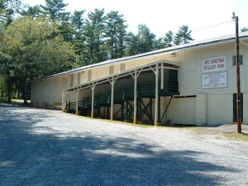 Exterior view of the Mt. Gretna Roller Rink, featuring a sloped entrance and surrounded by trees. Gravel path in foreground.