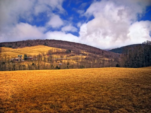 A scenic landscape featuring rolling hills, a grassy field, and a cloudy blue sky.