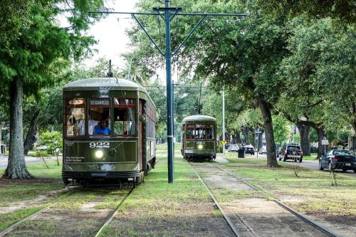 Two vintage streetcars on tracks surrounded by trees, with one streetcar approaching the other in a scenic area.