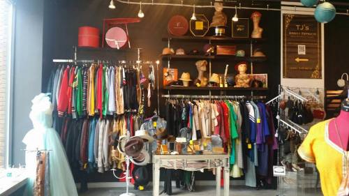 A colorful clothing store display featuring racks of clothes, hats, and accessories against a dark wall.