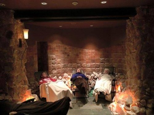 Three people relax in reclining chairs surrounded by salt walls and soft lighting in a tranquil spa setting.