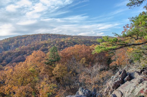 A scenic view of autumn foliage on rolling hills under a blue sky with wispy clouds.