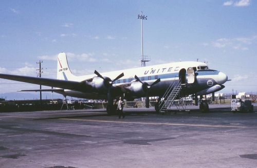 A vintage United Airlines airplane parked at an airport, with a staircase leading up to the entrance.