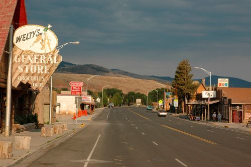 A quiet street scene featuring Welty's General Store, shops, and mountains in the background under a cloudy sky.