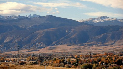 A scenic view of mountains with snow-capped peaks, rolling hills, and colorful autumn foliage in the foreground.