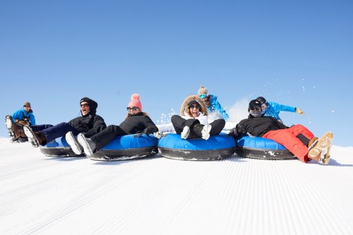A group of people enjoying snow tubing on a sunny day, laughing and having fun on blue inflatable tubes.