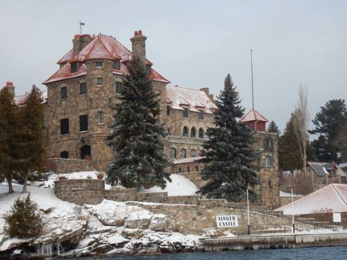 A large stone castle with a red-tiled roof, surrounded by snow-covered trees and a frozen lake.