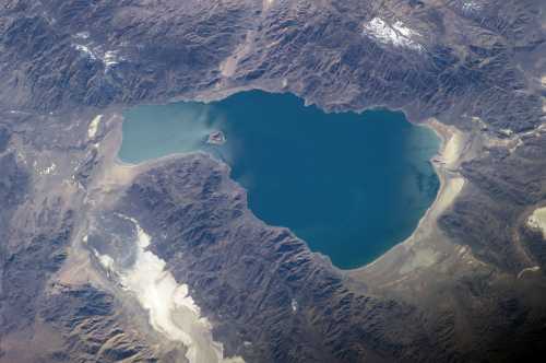 Aerial view of a large, blue lake surrounded by rugged mountains and rocky terrain.