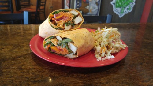 A plate with two wrapped sandwiches filled with vegetables and chicken, accompanied by a side of coleslaw.