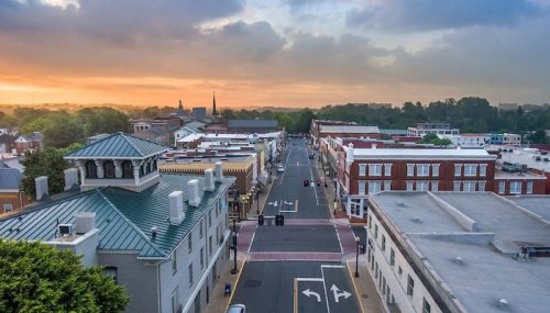 Aerial view of a small town street at sunrise, with buildings lining the road and a colorful sky in the background.