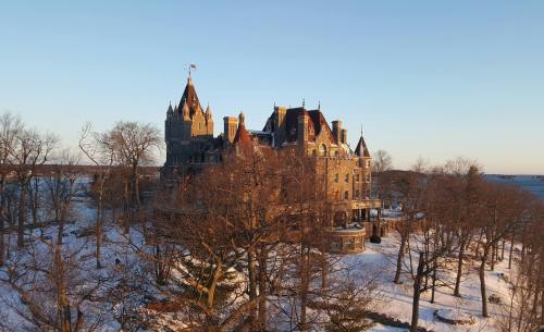 A grand, historic mansion surrounded by bare trees and snow, illuminated by the soft light of a setting sun.