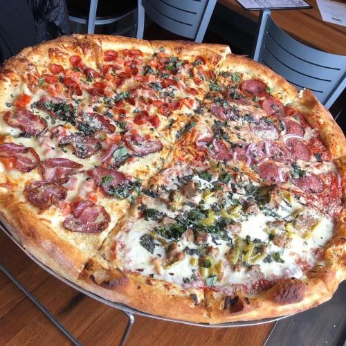 A large pizza divided into four sections, topped with various meats, vegetables, and herbs on a golden crust.