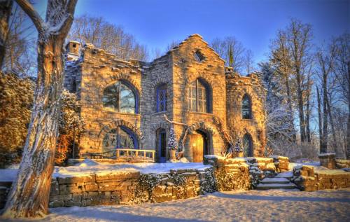 A stone mansion surrounded by snow-covered trees, bathed in warm sunlight during winter.