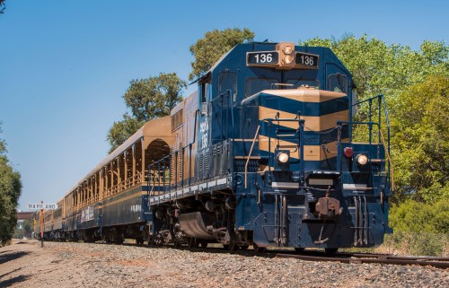 A blue and yellow train engine with passenger cars, stopped at a station named Haviland, surrounded by trees.