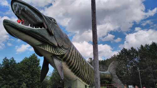 A giant fish sculpture with a wide open mouth, set against a blue sky and trees in the background.