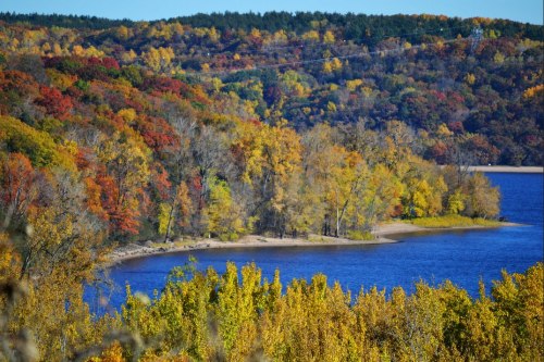 Vibrant autumn foliage surrounds a calm blue lake, with rolling hills in the background.