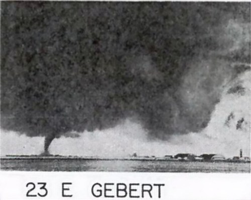 A dark, swirling tornado touches down near a landscape with buildings, labeled "23 E GEBERT."