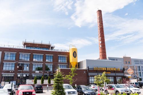 Exterior of Titletown Brewing Co. featuring a tall brick smokestack and a yellow water tower against a blue sky.