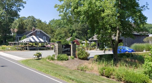 A scenic view of a garden center with a striped tent, surrounded by greenery and a blue car parked nearby.