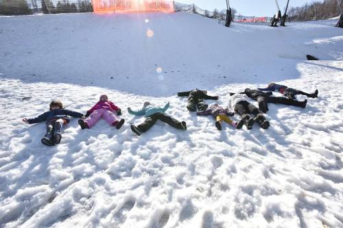 Children lying in the snow, making snow angels on a sunny winter day.